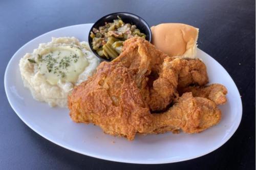 A plate of fried chicken with mashed potatoes, green beans, and a dinner roll.