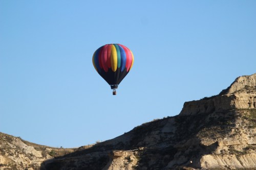 A colorful hot air balloon floats above a rocky landscape under a clear blue sky.