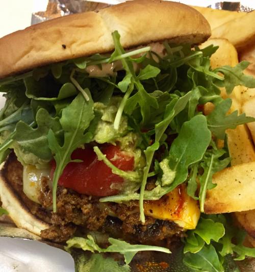 A close-up of a burger topped with lettuce, tomato, guacamole, and cheese, served with a side of fries.
