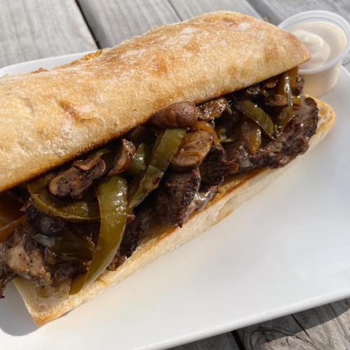 A hearty sandwich filled with grilled steak, sautéed mushrooms, and green peppers, served with a side of dipping sauce.