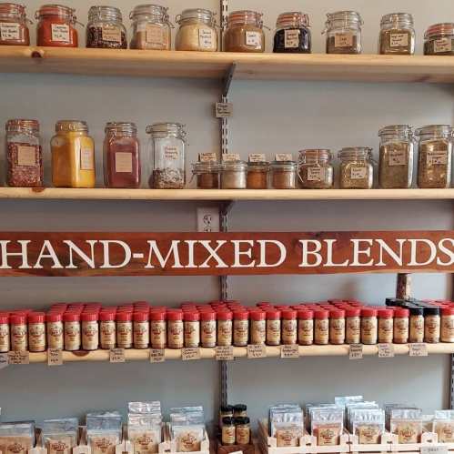 A shelf displaying various jars of spices and hand-mixed blends, labeled and organized neatly.