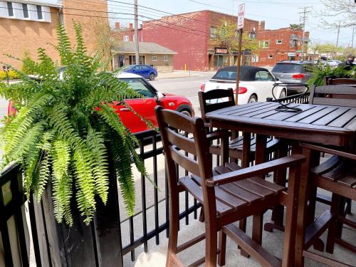 A view from a patio with wooden furniture and a large fern, overlooking a street with parked cars and buildings.