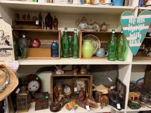 A display of vintage items, including green glass bottles, pottery, wooden boxes, and various collectibles on shelves.