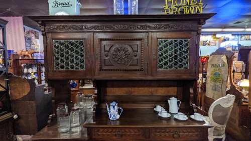 Antique wooden sideboard with intricate carvings and decorative glass panels, displayed in a vintage shop.