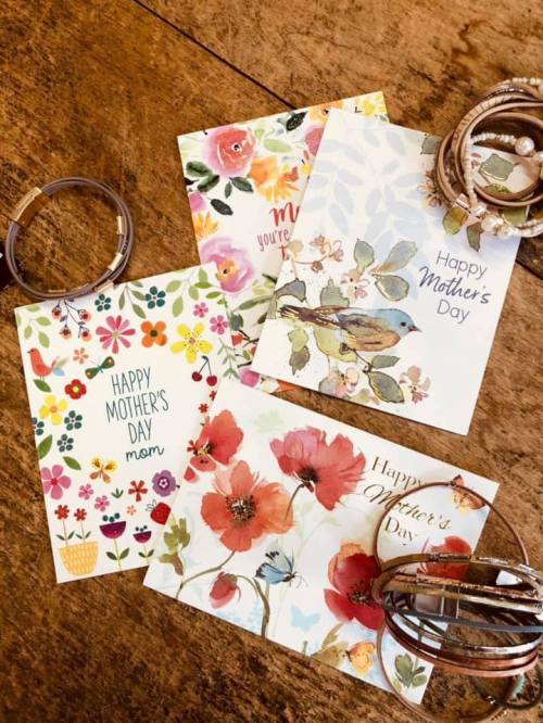 A collection of colorful Mother's Day cards arranged on a wooden surface, accompanied by bracelets.