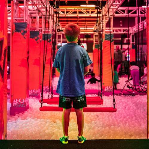 A child stands in front of colorful swings in a playful indoor space filled with soft balls.