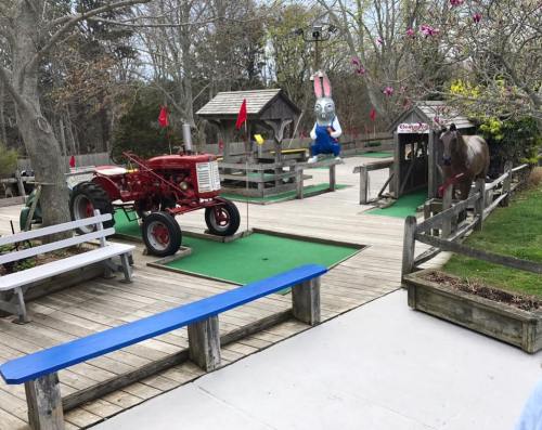 A mini-golf area featuring a red tractor, a horse statue, and a large bunny figure, surrounded by wooden structures.