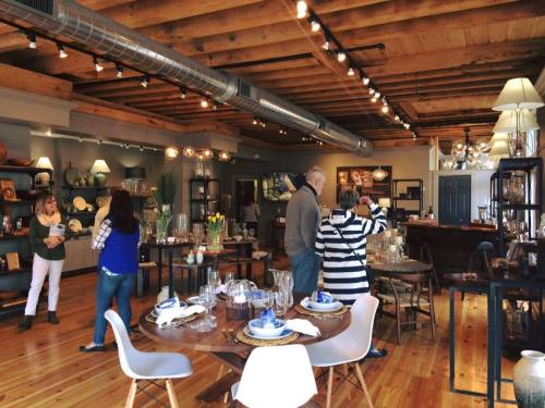 A stylish home decor store with wooden floors, showcasing tables, lamps, and decorative items, with customers browsing.