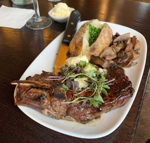 A plated meal featuring a grilled steak, baked potato with butter, sautéed mushrooms, and fresh herbs.