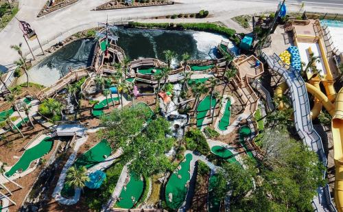 Aerial view of a mini-golf course with water features, surrounded by palm trees and slides in a recreational area.