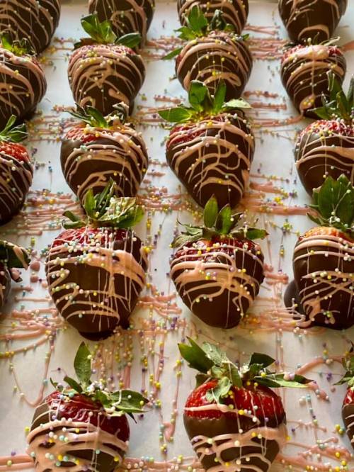 A close-up of chocolate-covered strawberries drizzled with pink icing and sprinkled with colorful decorations.