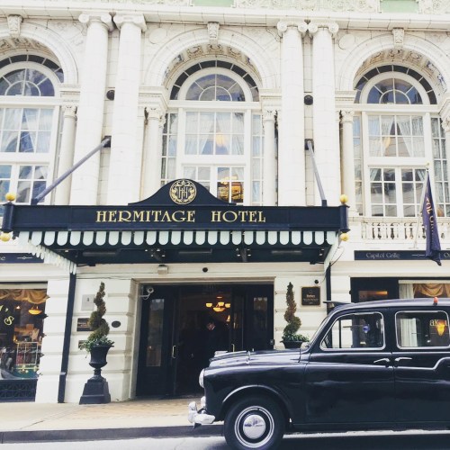 Exterior of the Hermitage Hotel featuring classic architecture and a vintage black taxi parked in front.