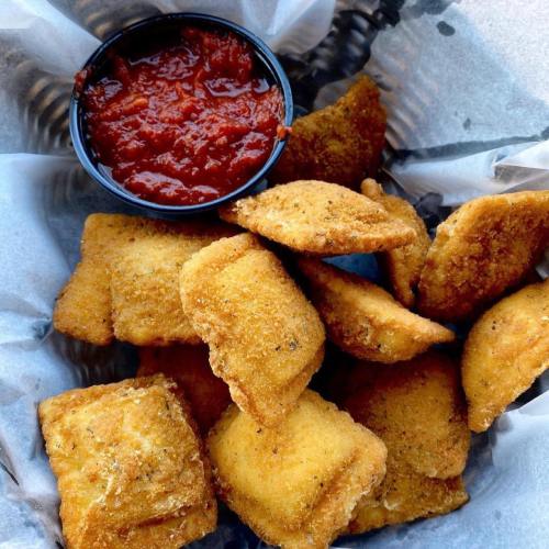A basket of golden-brown fried snacks with a small cup of marinara sauce on the side.