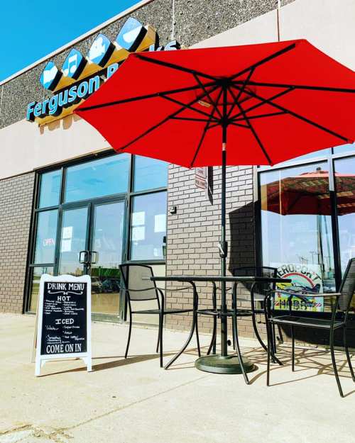 A red umbrella shades outdoor seating in front of Ferguson's, with a sign displaying the drink menu.