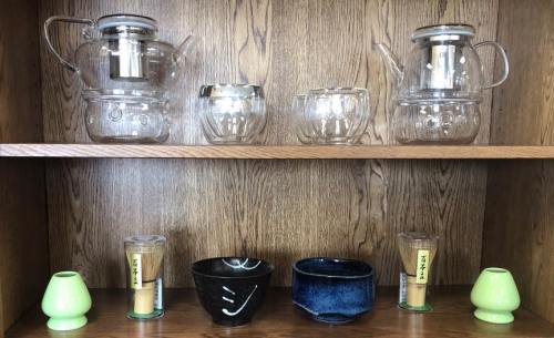 A wooden shelf displaying various glass teapots, bowls, and green candle holders.