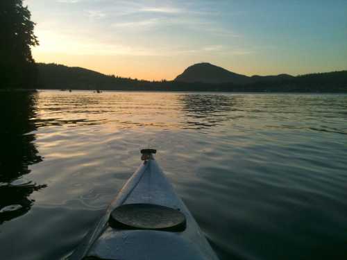 A kayak on calm water at sunset, with mountains and trees in the background.