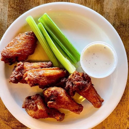 A plate of crispy chicken wings with celery sticks and a small cup of ranch dressing.