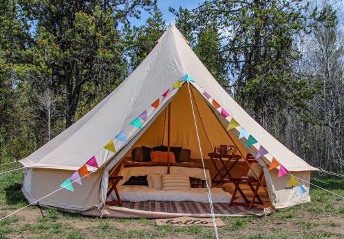 A cozy glamping tent with colorful bunting, set in a forested area, featuring comfortable seating and a welcoming atmosphere.