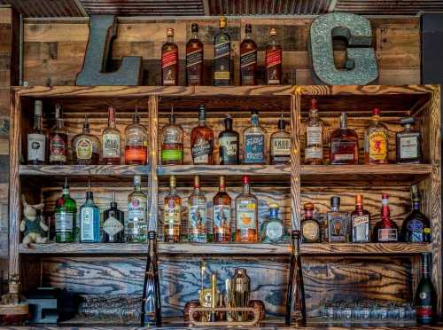 A wooden bar shelf displaying various bottles of liquor and spirits, with decorative letters "LMC" above.