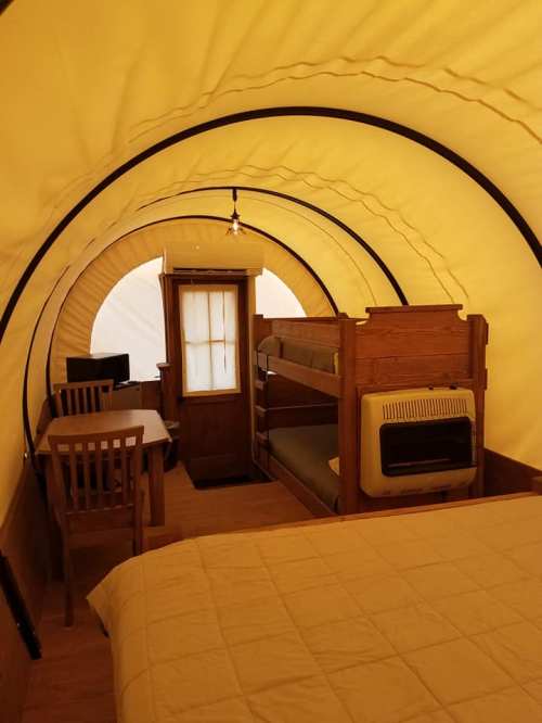 Interior of a cozy tent with a bunk bed, a desk, and a heater, featuring yellow fabric walls and wooden furniture.