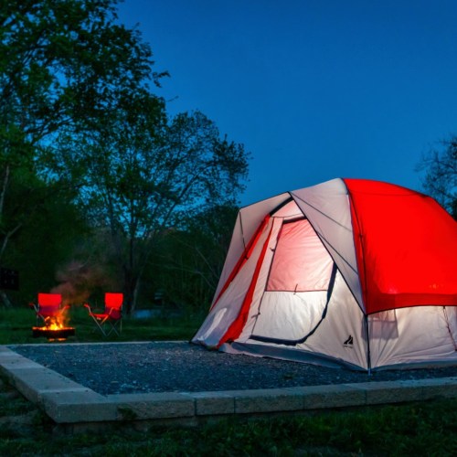 A red and white tent set up near a campfire, surrounded by trees in a serene outdoor setting.