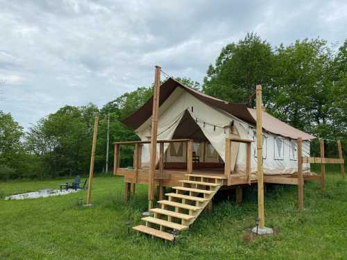 A glamping tent on a wooden platform surrounded by greenery, with steps leading up and a fire pit nearby.