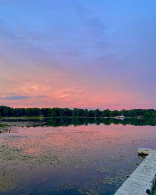 A serene lake at sunset, reflecting vibrant pink and purple hues in the sky, surrounded by lush greenery.