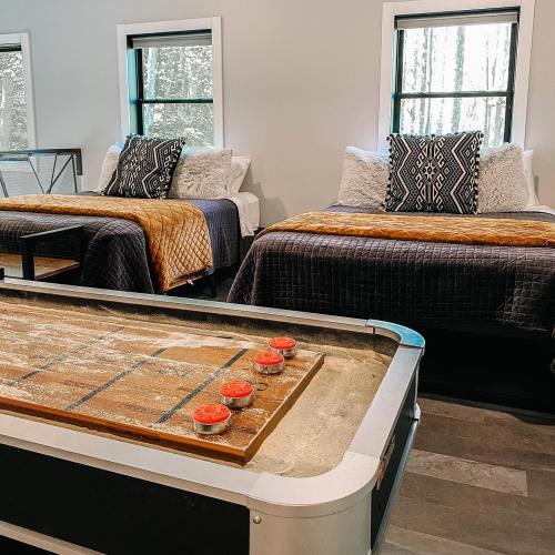 Cozy room with two beds, decorative pillows, and a shuffleboard table in a bright, nature-inspired setting.