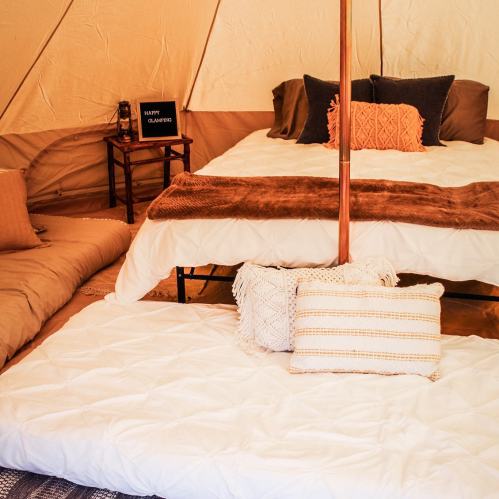Cozy tent interior with a bed, cushions, and decorative pillows, creating a warm and inviting atmosphere.