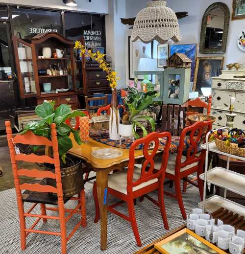 A cozy vintage shop interior featuring a colorful dining table, chairs, plants, and various decorative items.
