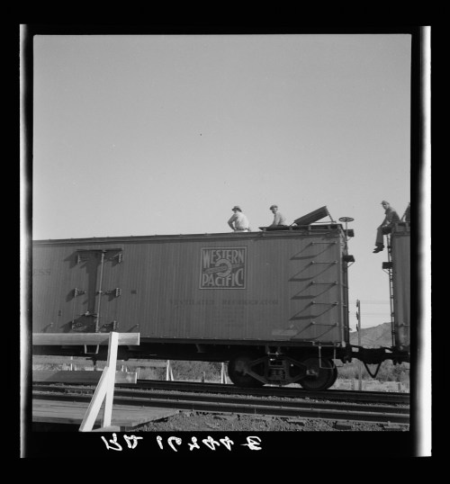 Two men sit on top of a Western Pacific train car against a clear sky.