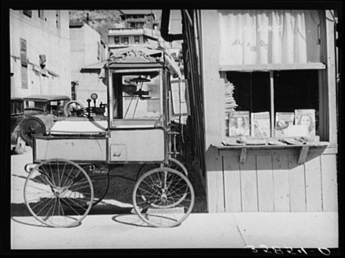 A vintage cart parked beside a wooden building with a window displaying magazines.