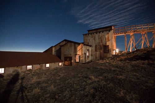 Abandoned industrial building at night, illuminated by soft light, with a clear sky and faint clouds above.