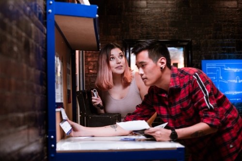 A man and woman interact at a counter, with the woman looking up and the man focused on paperwork.