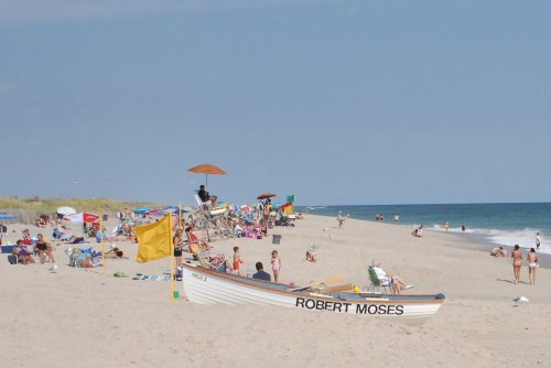 A beach scene with people sunbathing, colorful umbrellas, and a boat named "Robert Moses" on the sandy shore.