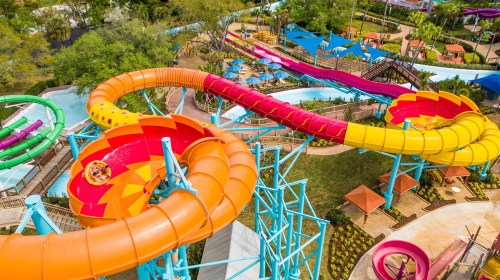 Aerial view of colorful water slides winding through a lush, landscaped water park.