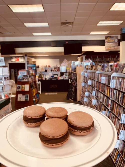 A plate of macarons in a bookstore, with shelves of books and a checkout area in the background.