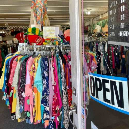 A colorful display of clothing hangs in a shop, with an "OPEN" sign visible at the entrance.