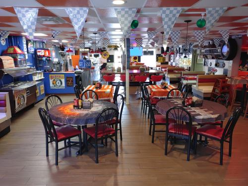 A colorful diner interior with checkered decor, empty tables, and racing-themed decorations.