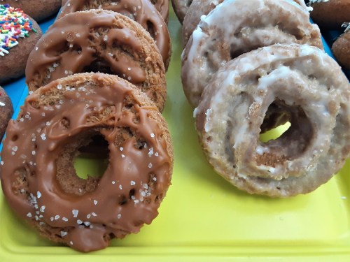 A colorful assortment of donuts, including chocolate frosted and glazed varieties, displayed on a yellow tray.