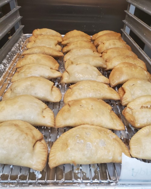A tray of golden-brown, freshly baked empanadas arranged in neat rows.