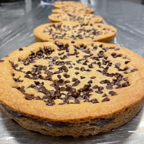 A row of round cookies topped with chocolate chips on a shiny surface.