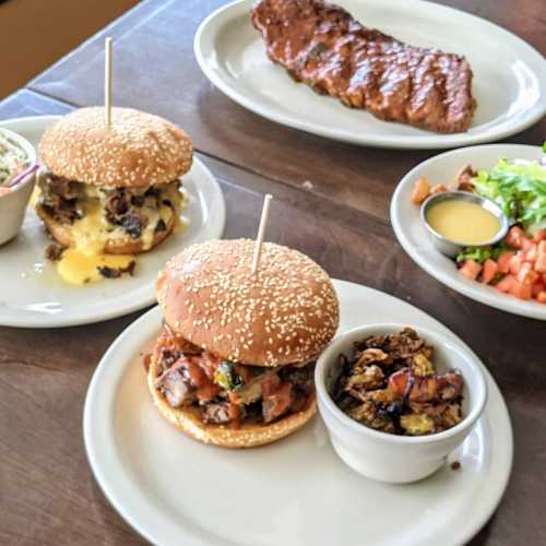 A table with two burgers, a plate of ribs, and a side salad with dressing.