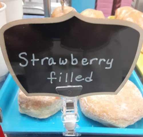 Sign displaying "Strawberry filled" in handwritten text, with baked goods in the background.
