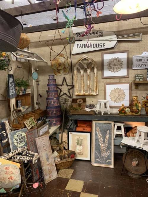 A cozy shop display featuring farmhouse decor, signs, and various decorative items arranged on shelves and tables.