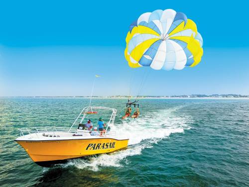 A colorful parasail being towed by a yellow boat on a clear blue ocean.