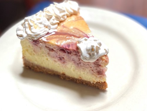 A slice of cheesecake topped with whipped cream and fruit, served on a white plate.