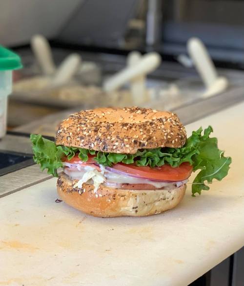 A sesame seed bagel sandwich filled with lettuce, tomato, and sliced meat on a countertop.