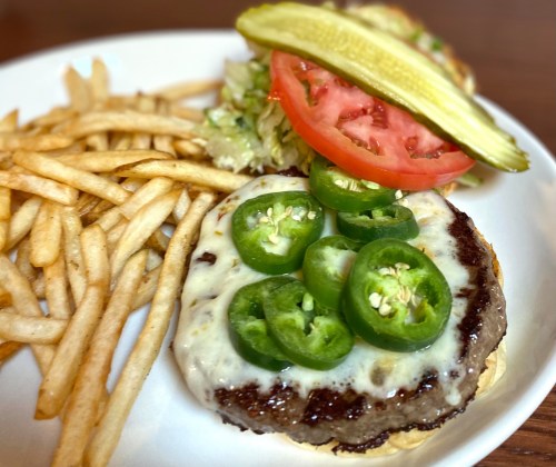A juicy burger topped with jalapeños, cheese, lettuce, tomato, and pickles, served with a side of crispy fries.