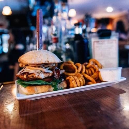 A delicious burger with melted cheese and lettuce, served with curly fries and a dipping sauce on a wooden table.
